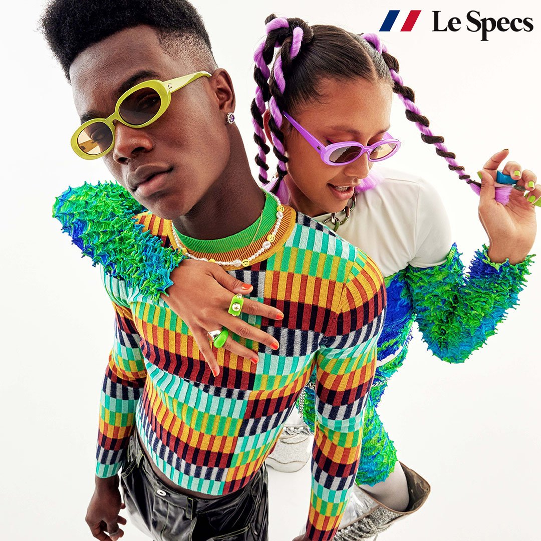 Fashion-forward eyewear ad featuring a Black male model and a biracial female model wearing colorful Le Specs sunglasses and vibrant outfits.