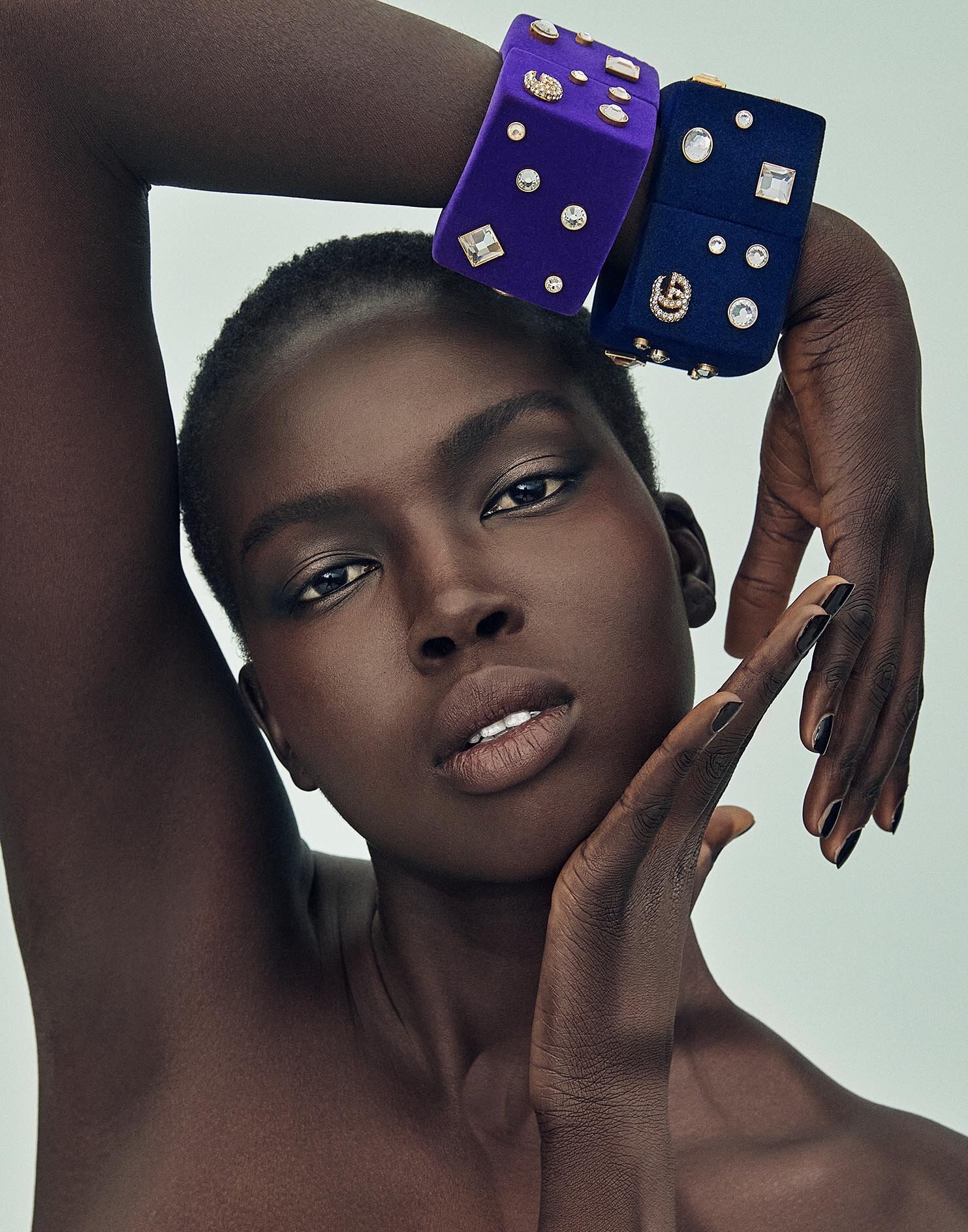 Dark-skinned woman poses with bejeweled purple and blue bracelets. Close-up fashion shot in a photo studio with a neutral backdrop.