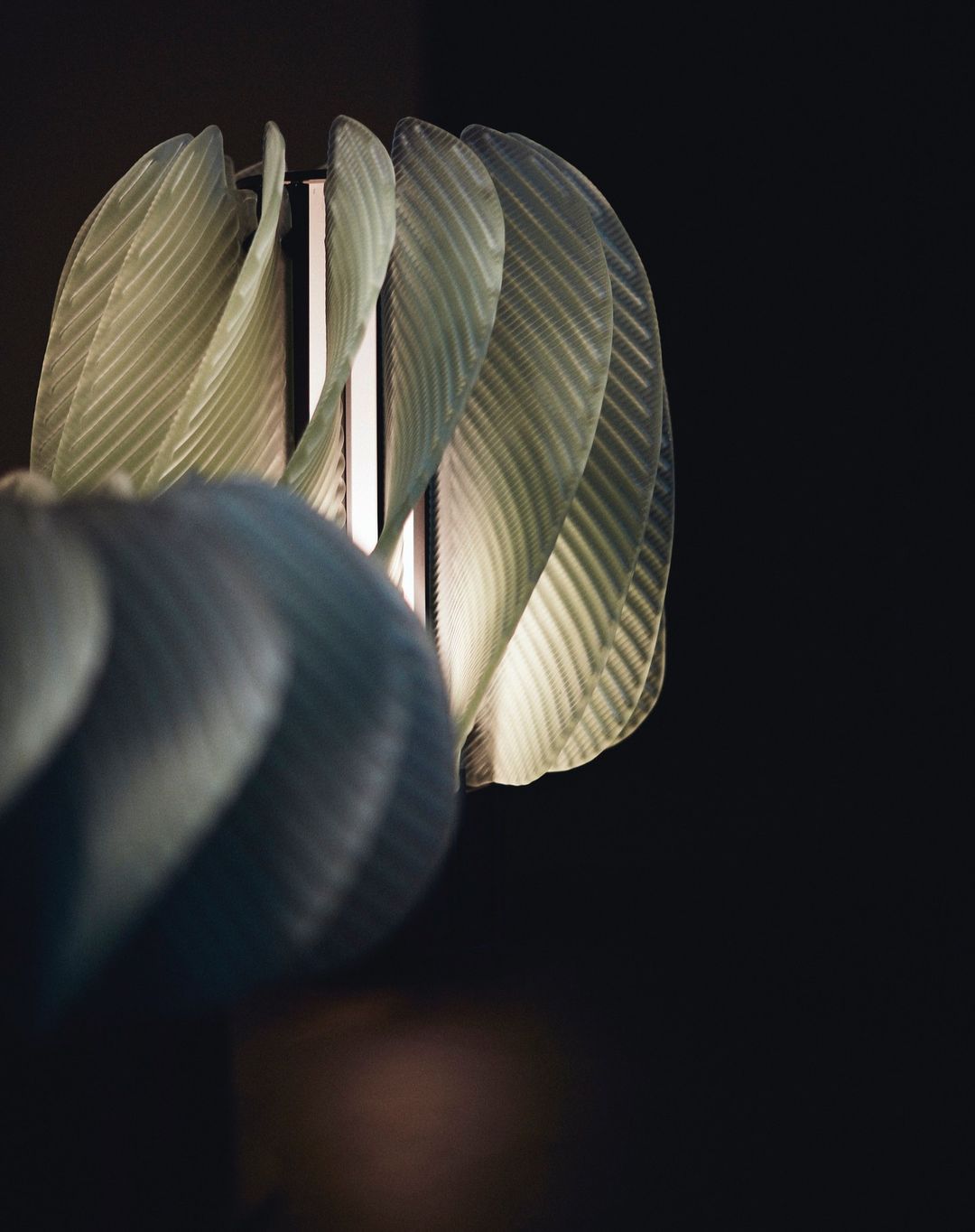 Indoor shot of a modern lamp featuring translucent, textured petals and a sleek metal frame against a dark, minimalist background.