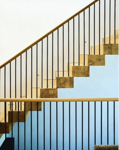 Architectural image of modern indoor staircase featuring wooden steps and black metal railing against white and light blue wall.