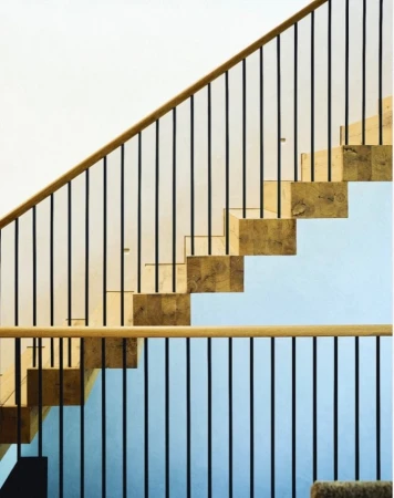 Architectural image of modern indoor staircase featuring wooden steps and black metal railing against white and light blue wall.