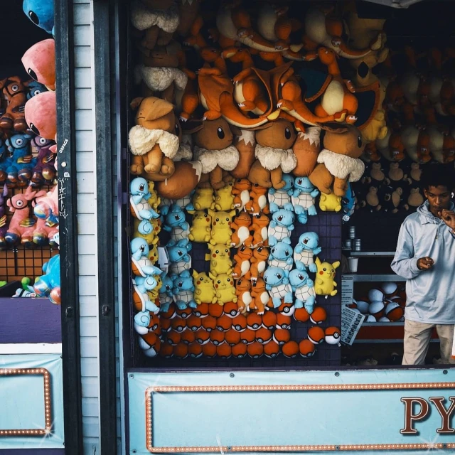 Eye-level shot of an adult male standing in front of a game booth, featuring a variety of Pokémon plush toys, providing a whimsical feel.