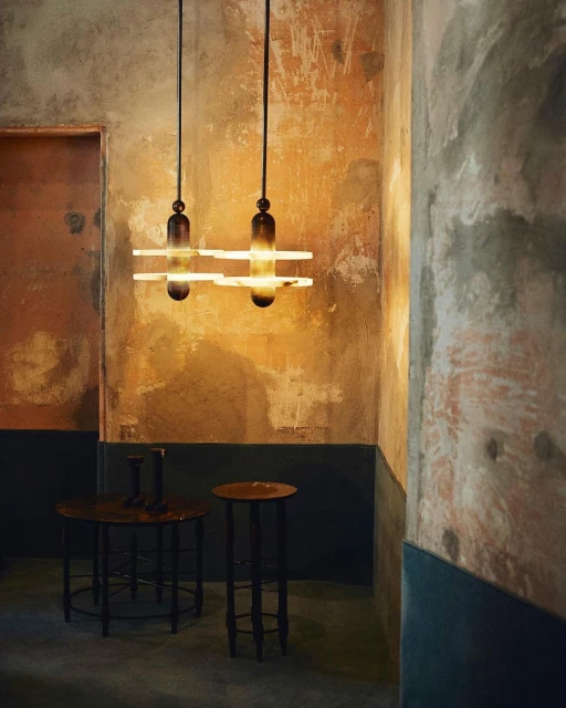 Interior view of a room featuring two pendant lights hanging above two small tables against textured walls. Decorative lighting.