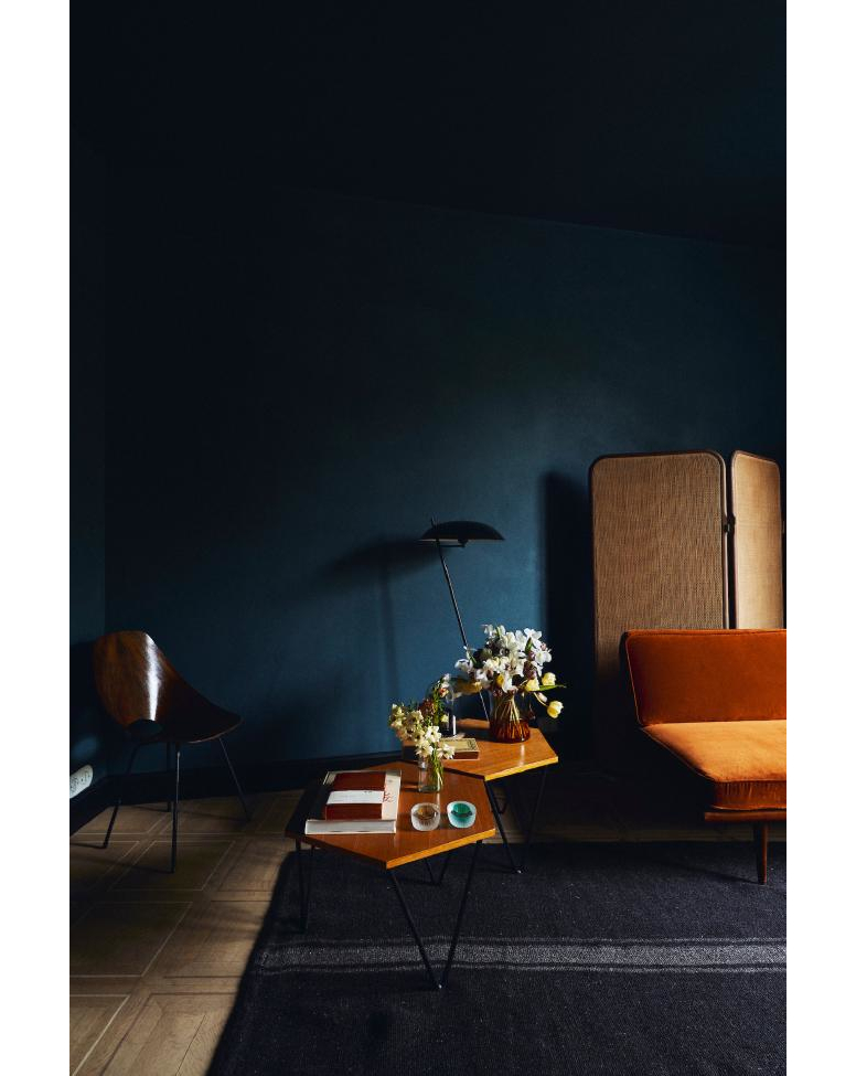 Interior space featuring a geometric side table with floral arrangements, a dark blue wall, a patterned rug, and a minimalist chair.