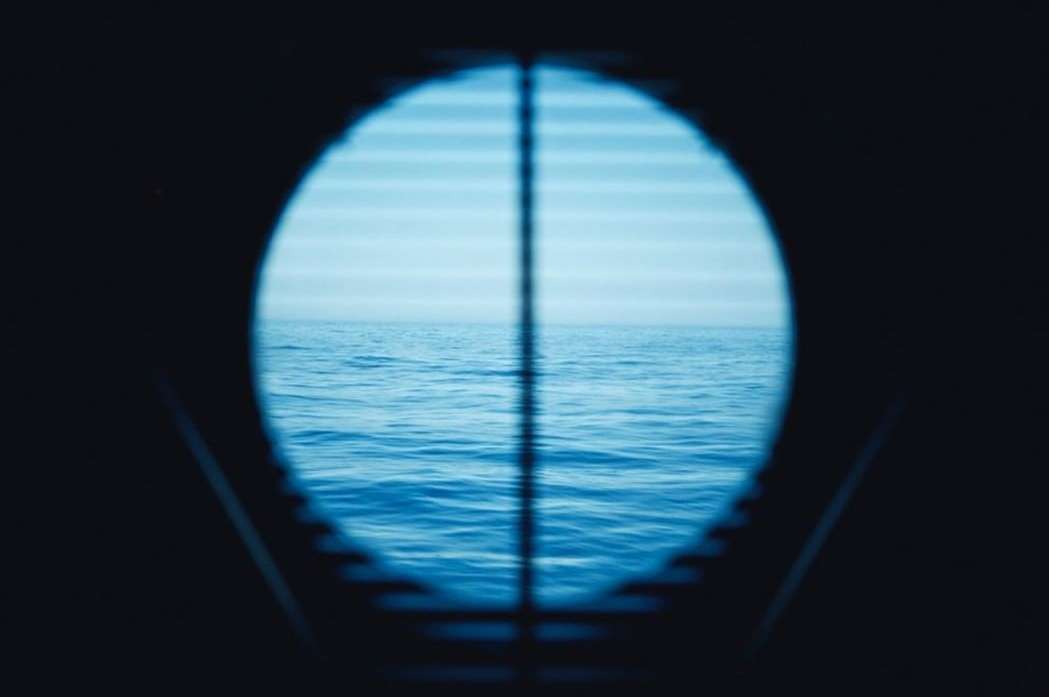 Ocean view framed through a blue-tinted porthole-style opening, capturing a serene seascape with slight waves and soft lighting.