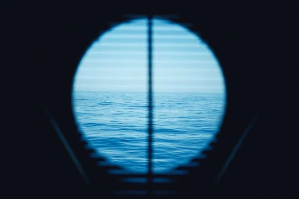 Ocean view framed through a blue-tinted porthole-style opening, capturing a serene seascape with slight waves and soft lighting.