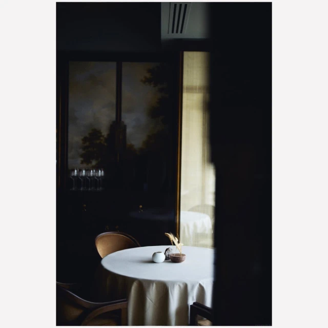 Elegant restaurant table setting with white tablecloth, glassware, and dark interior featuring a framed landscape painting.