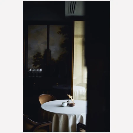 Elegant restaurant table setting with white tablecloth, glassware, and dark interior featuring a framed landscape painting.