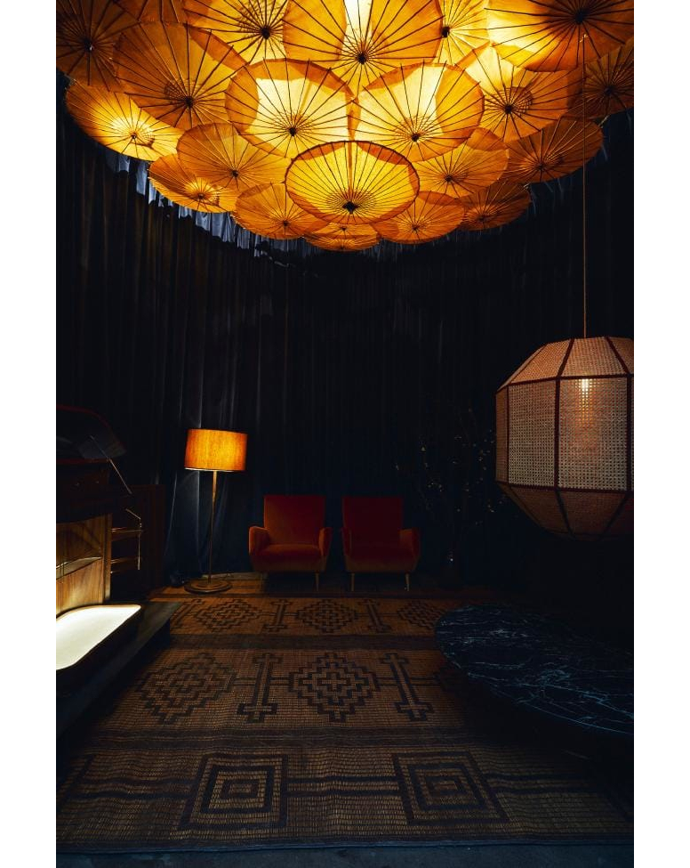 Interior room featuring vintage armchairs, a patterned area rug, hanging paper parasol lights, and lamps, creating a warm, inviting atmosphere.
