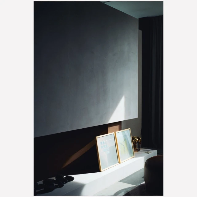 Interior view of a modern living space featuring a minimalist design with a textured gray wall, artwork, and soft, diffused light.