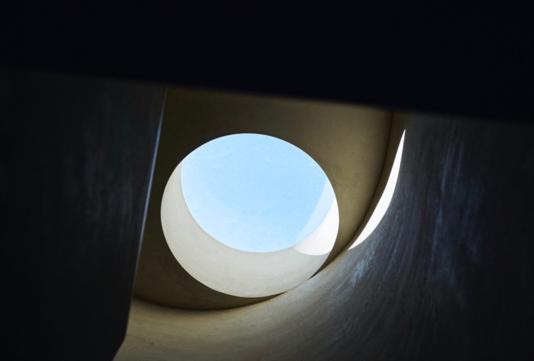 Abstract view looking up through a circular opening showing a bright blue sky, with architectural elements surrounding the opening.