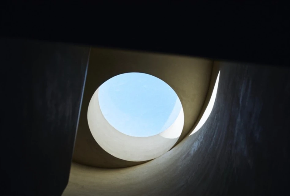 Abstract view looking up through a circular opening showing a bright blue sky, with architectural elements surrounding the opening.
