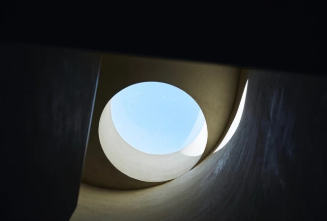 Abstract view looking up through a circular opening showing a bright blue sky, with architectural elements surrounding the opening.