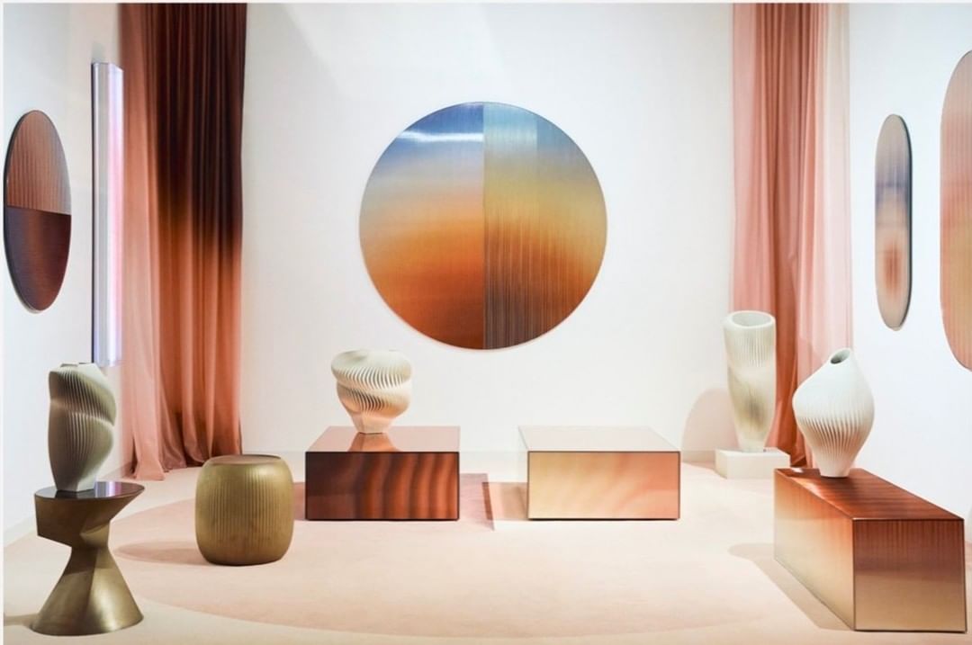 Interior design featuring vases displayed on plinths with circular artworks, ombre curtains, and neutral backdrop, creating a gallery-like setting.