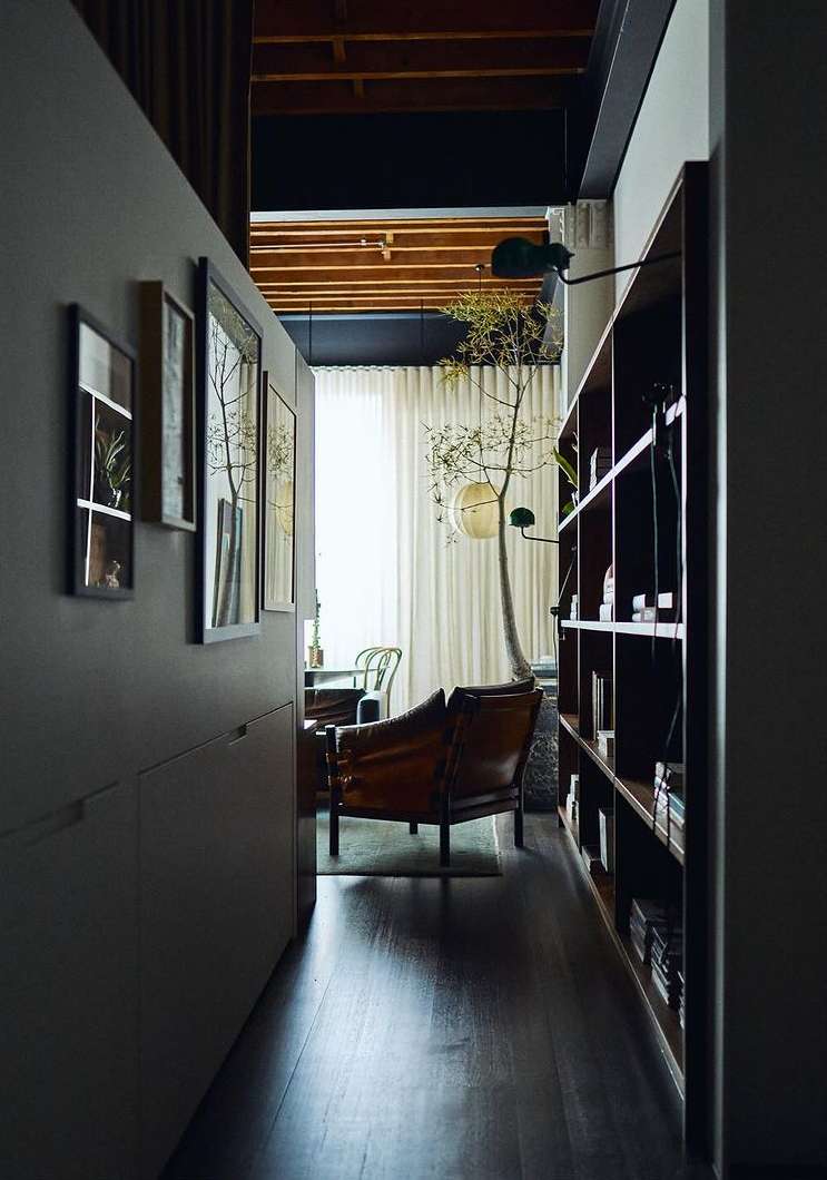 Home interior with a leather armchair, bookshelf, hardwood floors, and natural lighting showcasing a minimalist design and neutral tones.