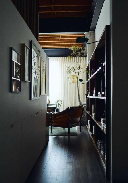 Home interior with a leather armchair, bookshelf, hardwood floors, and natural lighting showcasing a minimalist design and neutral tones.