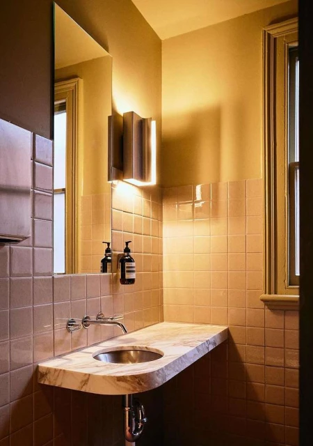 Interior bathroom view features a marble countertop sink, modern lighting, and tiled walls creating a clean, stylish aesthetic.