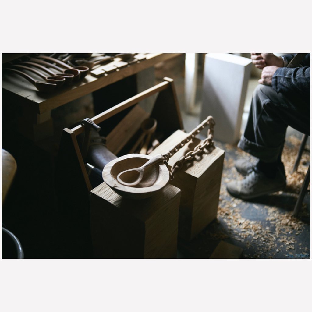 Hand-carved wooden bowl and spoon, displaying artisan craftsmanship, next to a carpenter working in a workshop with rustic wooden tools.