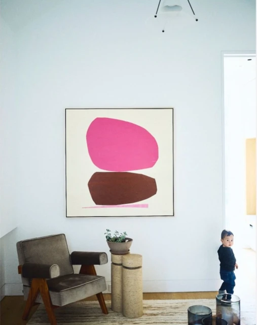Living room interior featuring an abstract art painting, a gray armchair, a cylinder side table, and a toddler in the background.
