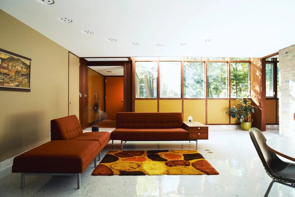 Living room interior with brown sectional sofa, rug with brown and orange geometric patterns, and large windows with a view of trees.