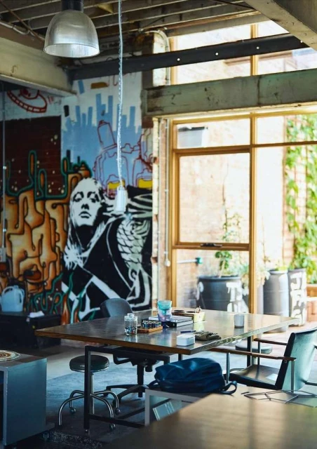 Creative work space featuring a wooden table with various items, chairs, and a painted wall with a window letting in natural light.