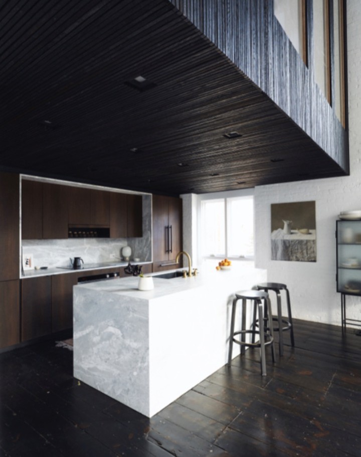 Modern kitchen interior featuring a marble island with stools, dark wood cabinets, and a high ceiling with unique architectural details.
