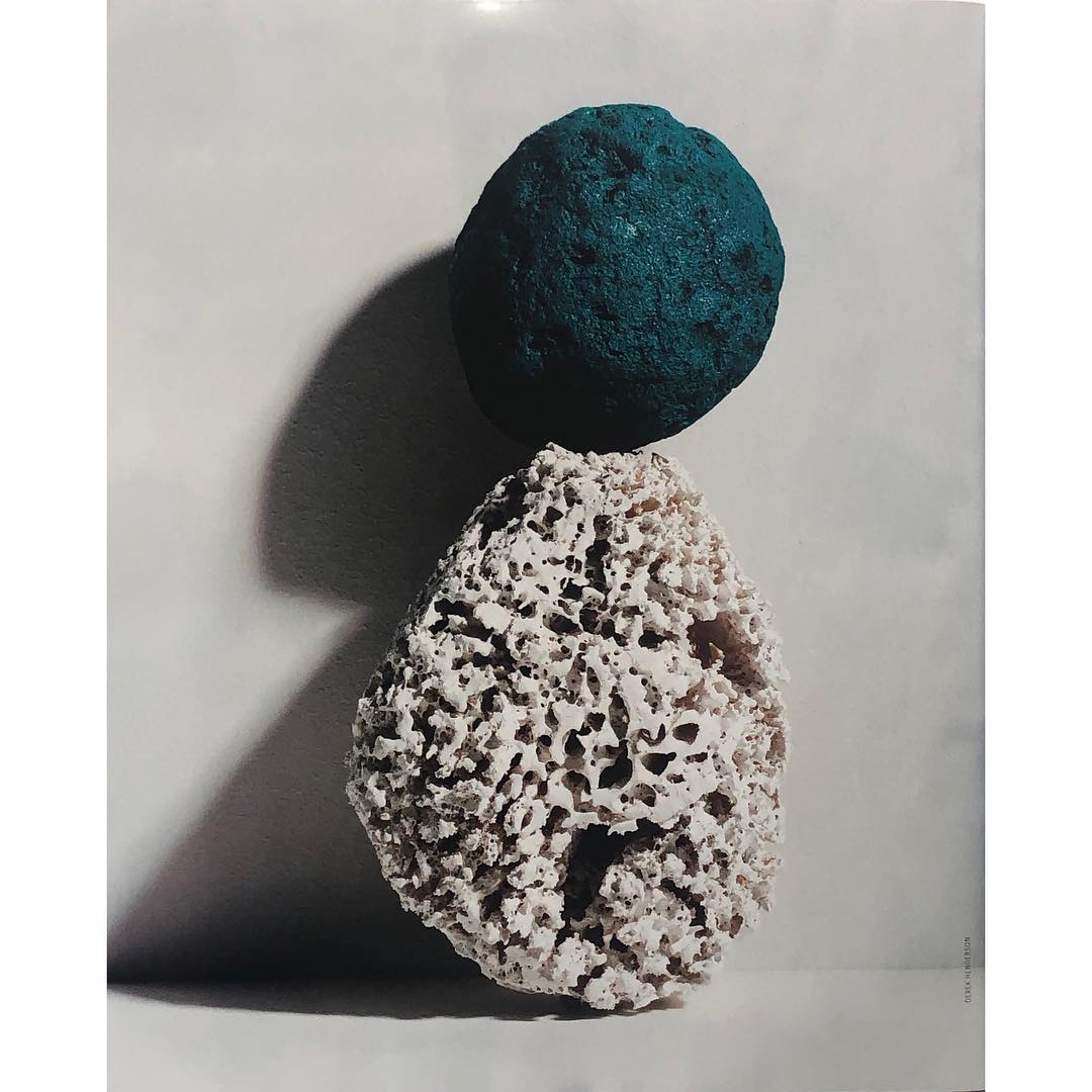 Still life studio shot of stacked rock-like objects, one teal, one porous beige. Soft lighting and subtle shadowing create depth and texture.