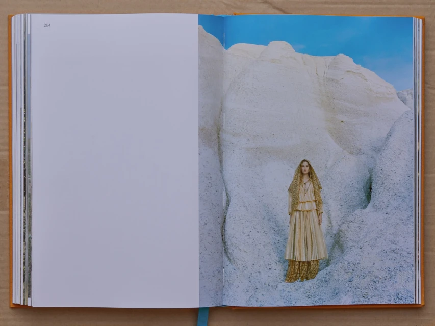 Fashion photo shoot in an open book, featuring a woman in a layered dress amidst white rock formations against a blue sky backdrop.