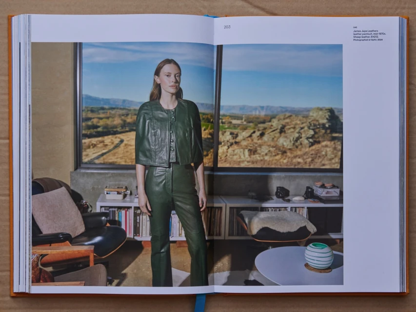 Woman in a green leather jacket and pants stands in front of a window with a mountain view, styled for a fashion editorial.