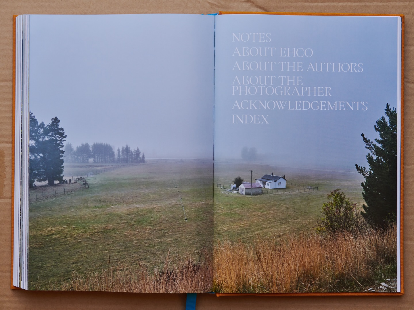 Open book featuring a landscape photograph with a farmhouse, fields, and trees under a foggy sky, accompanied by text on the opposite page.
