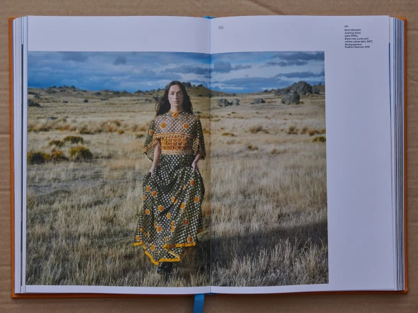 Open book spread showing a fashion photograph of a woman walking across a dry grassy field under a cloudy sky.