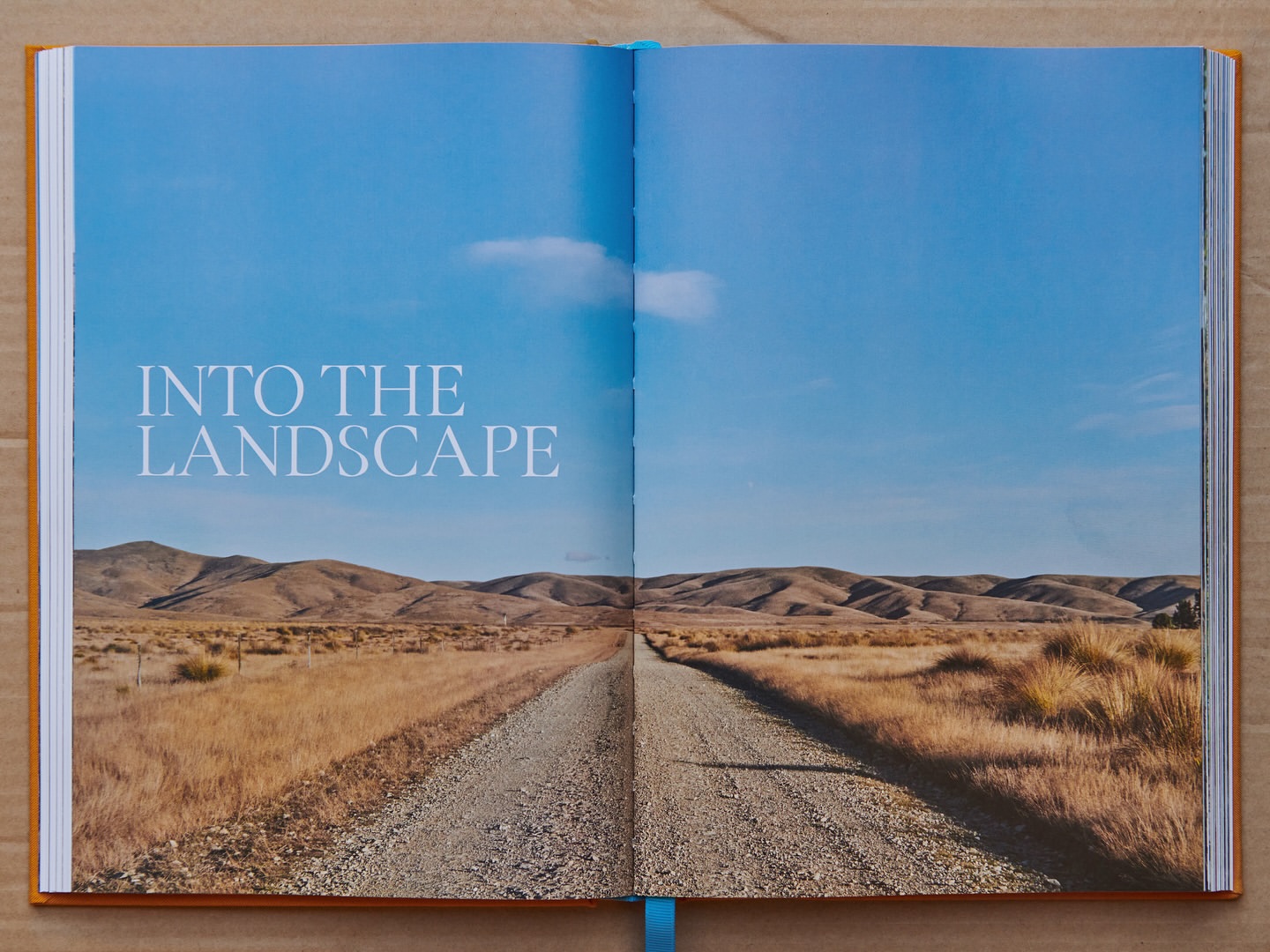 Open book displaying a landscape photograph of a gravel road leading to hills under a clear blue sky, evoking a sense of travel.