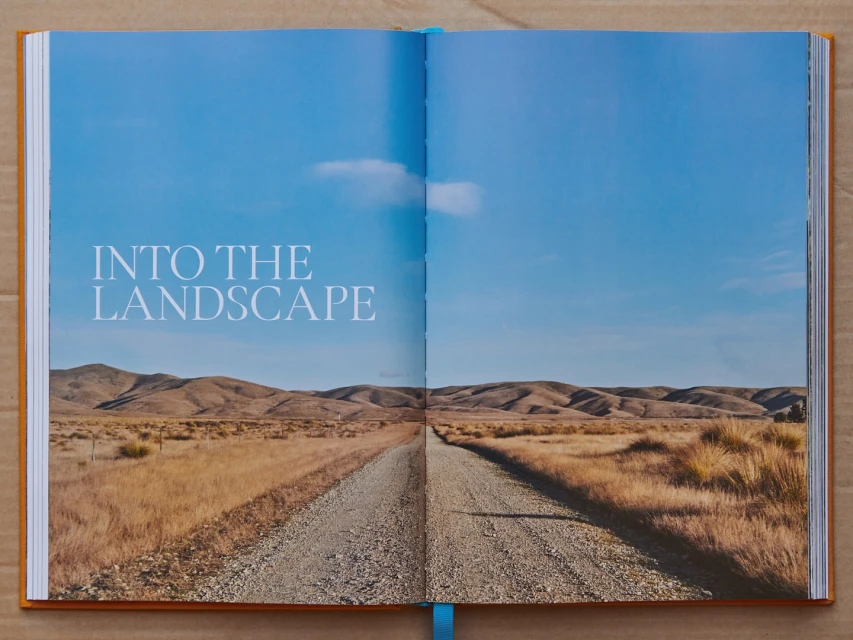 Open book displaying a landscape photograph of a gravel road leading to hills under a clear blue sky, evoking a sense of travel.