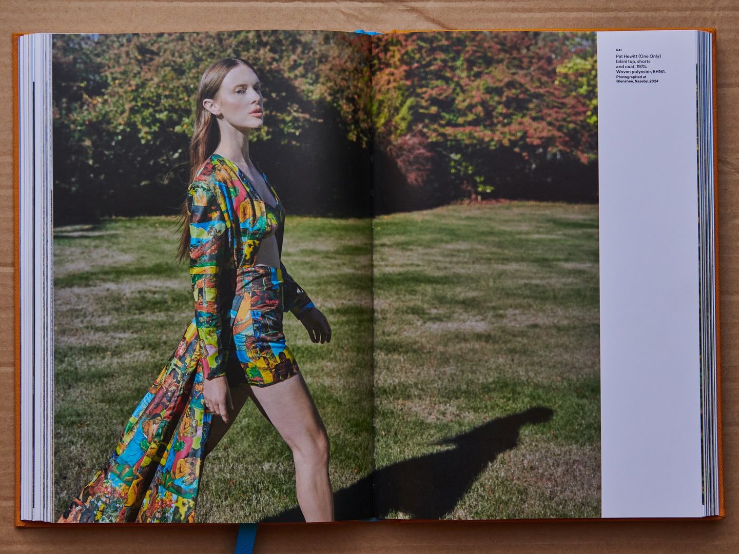 Fashion editorial shot in a garden, featuring a model in a printed two-piece set with a matching coat, posing on grass in daylight.