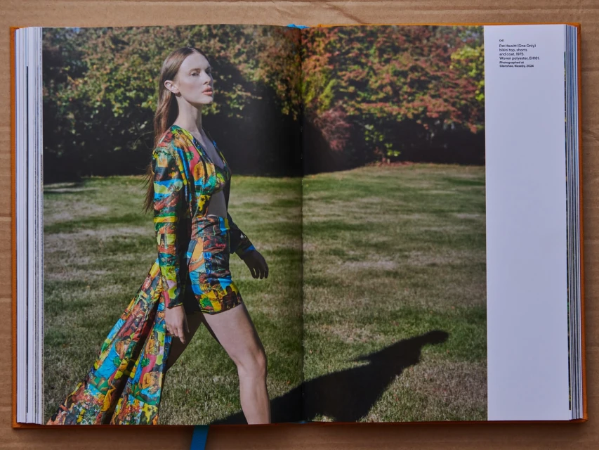 Fashion editorial shot in a garden, featuring a model in a printed two-piece set with a matching coat, posing on grass in daylight.