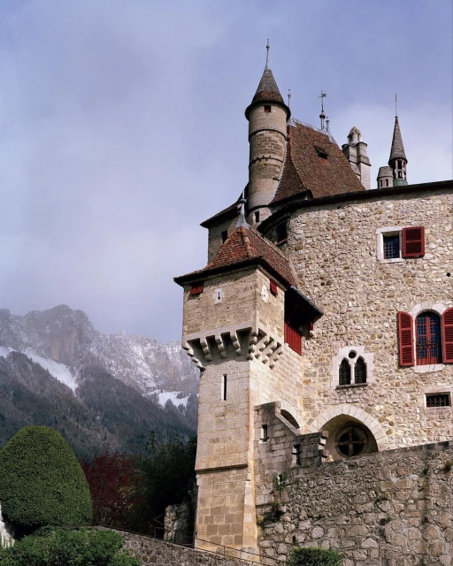 A view of Chillon Castle, a medieval fortress on Lake Geneva, Switzerland with red shutters and roof tiles in a cloudy setting.