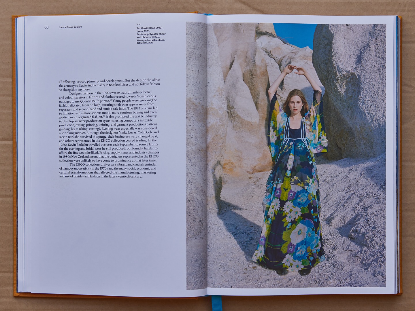 Fashion editorial in open book features a woman in a floral dress, standing amid rock formations under a clear sky, artistic layout.