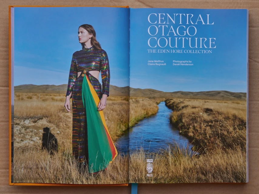 Open book featuring a fashion photograph of a model in a colorful dress in a field and a landscape with a river and mountains.