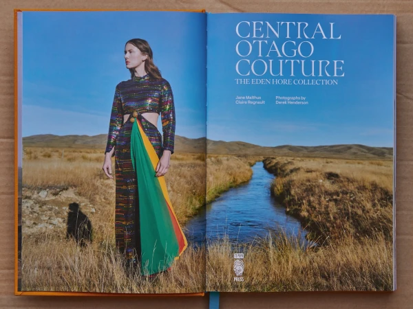Open book featuring a fashion photograph of a model in a colorful dress in a field and a landscape with a river and mountains.