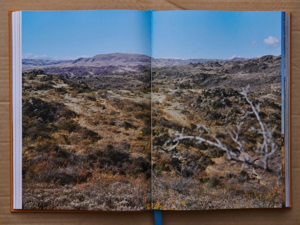 An open photo book resting on brown paper, showing a landscape photograph of arid hills and sparse vegetation.