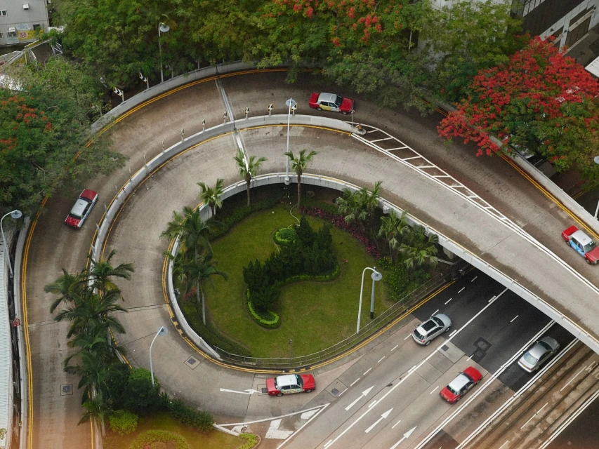 High-angle view of several cars on a winding road and a straight road, with lush green vegetation in the center island.