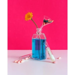 Clear glass bottle with blue liquid holding a yellow flower and a funnel with pills, against a pink background.