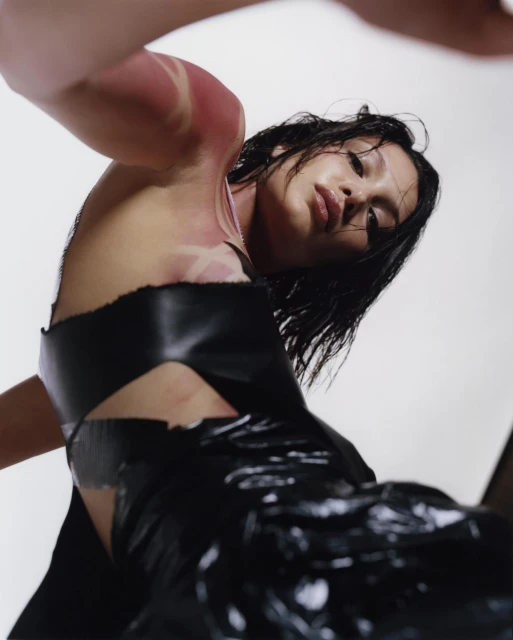 Adult female with wet black hair in dark avant-garde fashion dress, shot at a low angle in a photo studio against a white background.