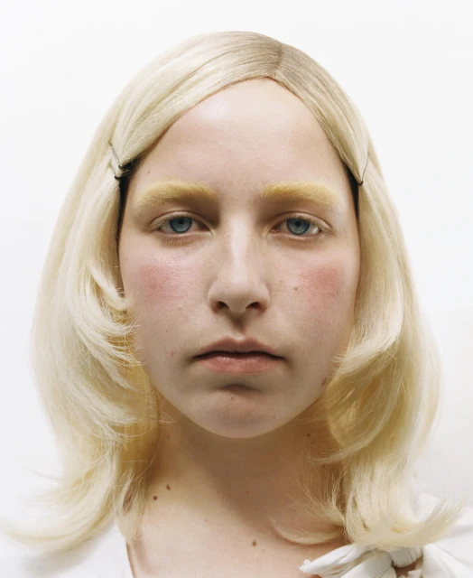 Close-up portrait of a blonde adult female in white top, with fair complexion and light blue eyes, posed in front of a white backdrop.