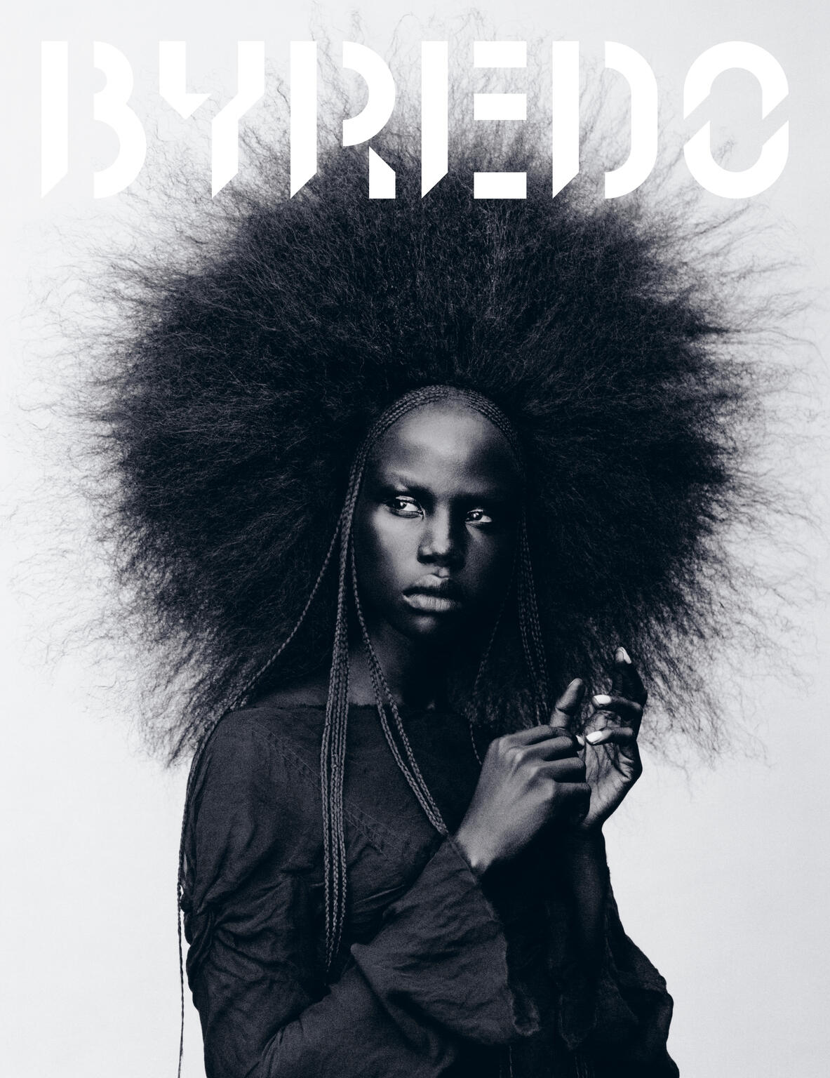 Striking black and white portrait of a woman with a voluminous afro hairstyle, wearing a dark top, against a light backdrop. 