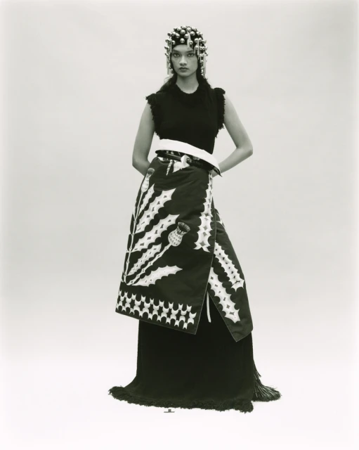 Monochrome fashion portrait of a female model with an elaborate headpiece, sleeveless top, and wrap skirt with thistle design.