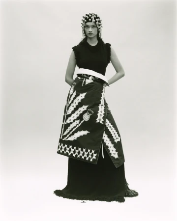 Monochrome fashion portrait of a female model with an elaborate headpiece, sleeveless top, and wrap skirt with thistle design.