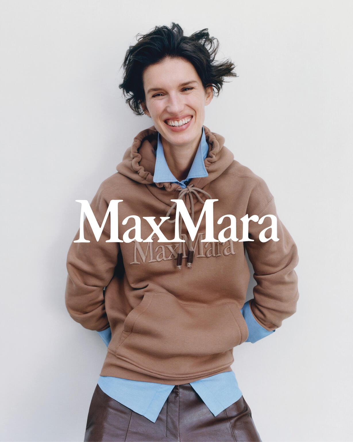 Smiling model wearing a brown hoodie over a light blue collared shirt against a white background