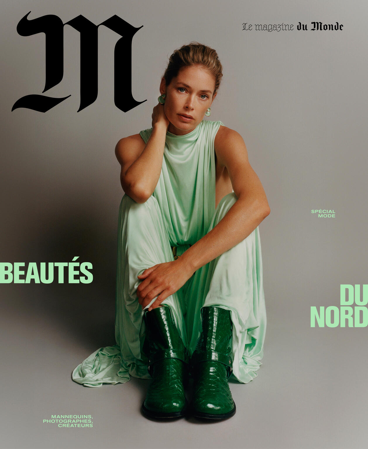Fashion magazine cover featuring a female model in a green dress and boots, sitting on the floor against a grey background.