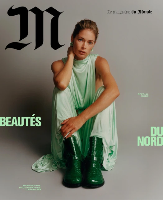 Fashion magazine cover featuring a female model in a green dress and boots, sitting on the floor against a grey background.